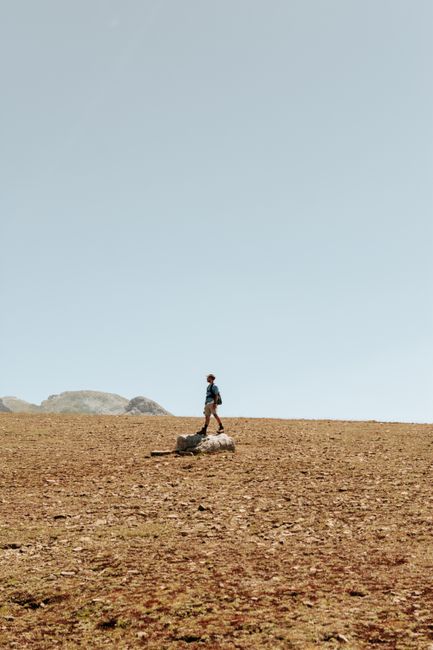 A solitary hiker walks across an expansive desert landscape, embracing outdoor adventure.