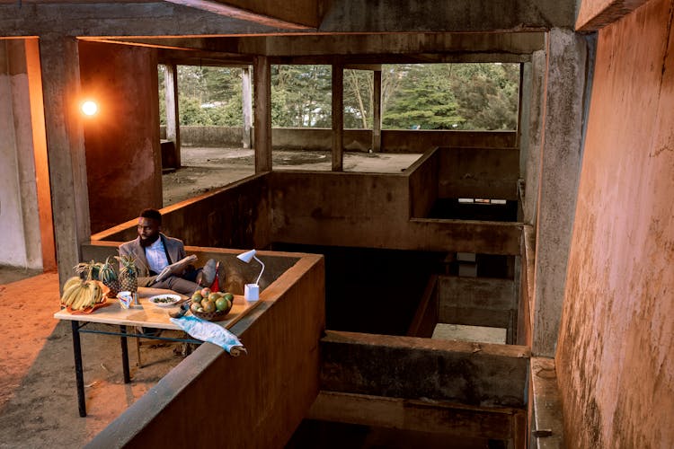 Man Sitting By Desk With Fruits At Abandoned Construction Site