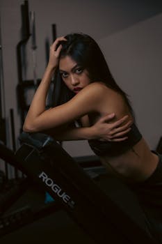 Confident woman in a gym posing on workout equipment during a fitness session.