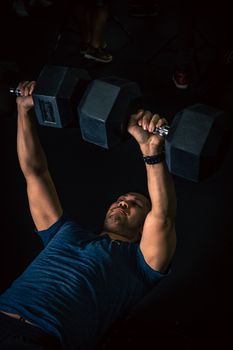 Muscular man lifting heavy dumbbells indoors showcasing strength and fitness.