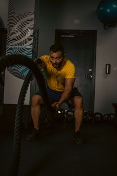 A determined man engages in an intense rope workout session in a modern gym setting.