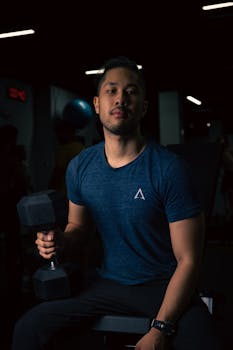 Focused young man working out with dumbbell in a dimly lit gym setting.