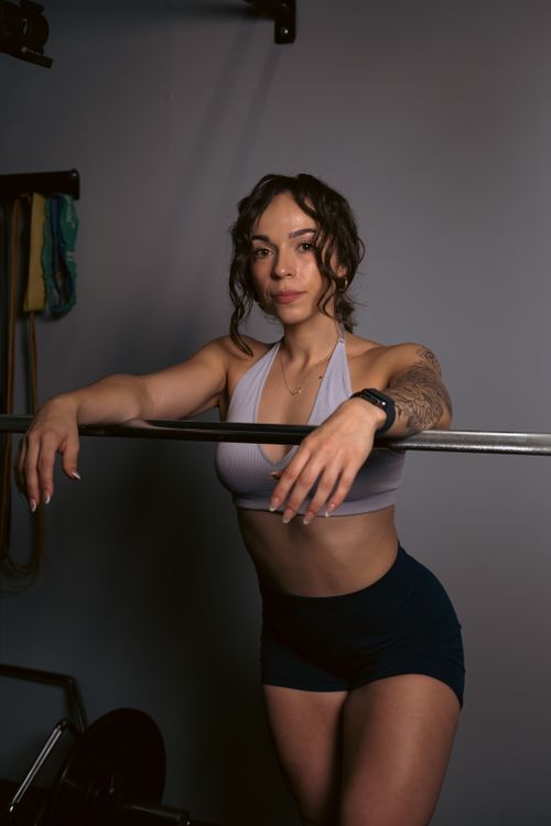 Free Confident woman in activewear posing with a barbell in an indoor gym environment. Stock Photo