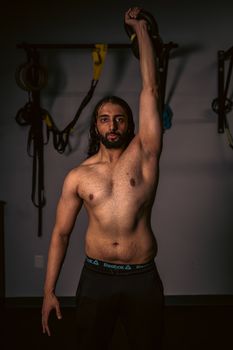 Shirtless man exercising with a kettlebell indoors, showcasing strength and fitness.