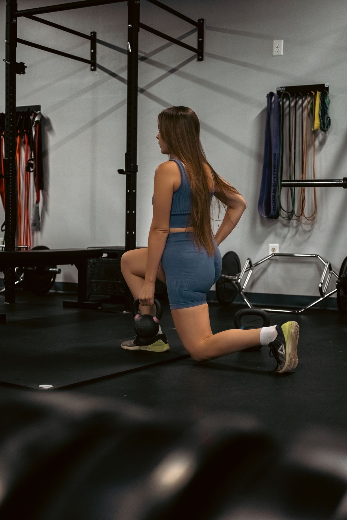 Woman performing a kettlebell lunge in a gym as part of a strength routine for runners