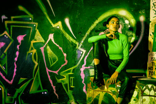 Free A fashionable young woman posing confidently against a colorful graffiti backdrop in an urban setting. Stock Photo