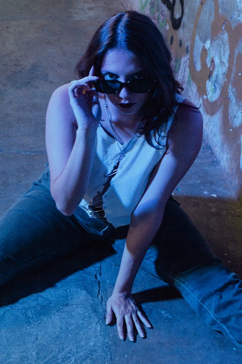 Woman in White Tank Top Wearing Sunglasses Sitting on Floor 