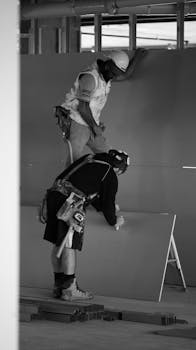 Monochrome capture of two construction workers assembling drywall inside a building site.