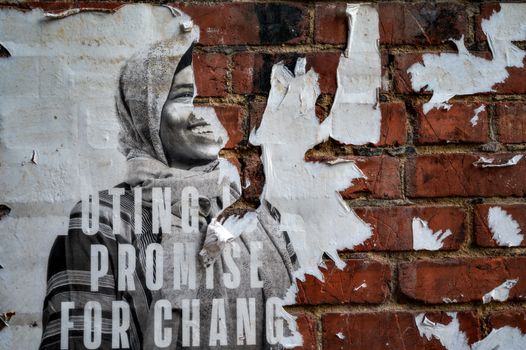 A weathered poster on brick wall reveals urban decay, depicting a smiling woman.