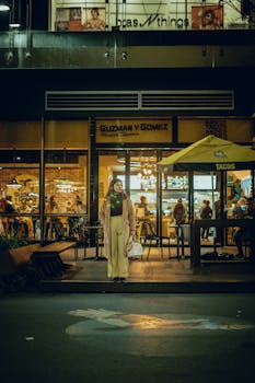 A woman in a pink coat stands outside a Guzman y Gomez in Canberra, Australia at night.