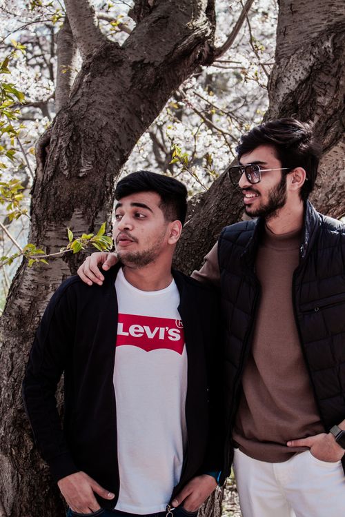 Free Two male friends enjoying a casual moment in a park during spring season, by a tree. Stock Photo
