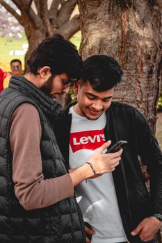 Two young men sharing a moment outdoors while browsing a smartphone together.