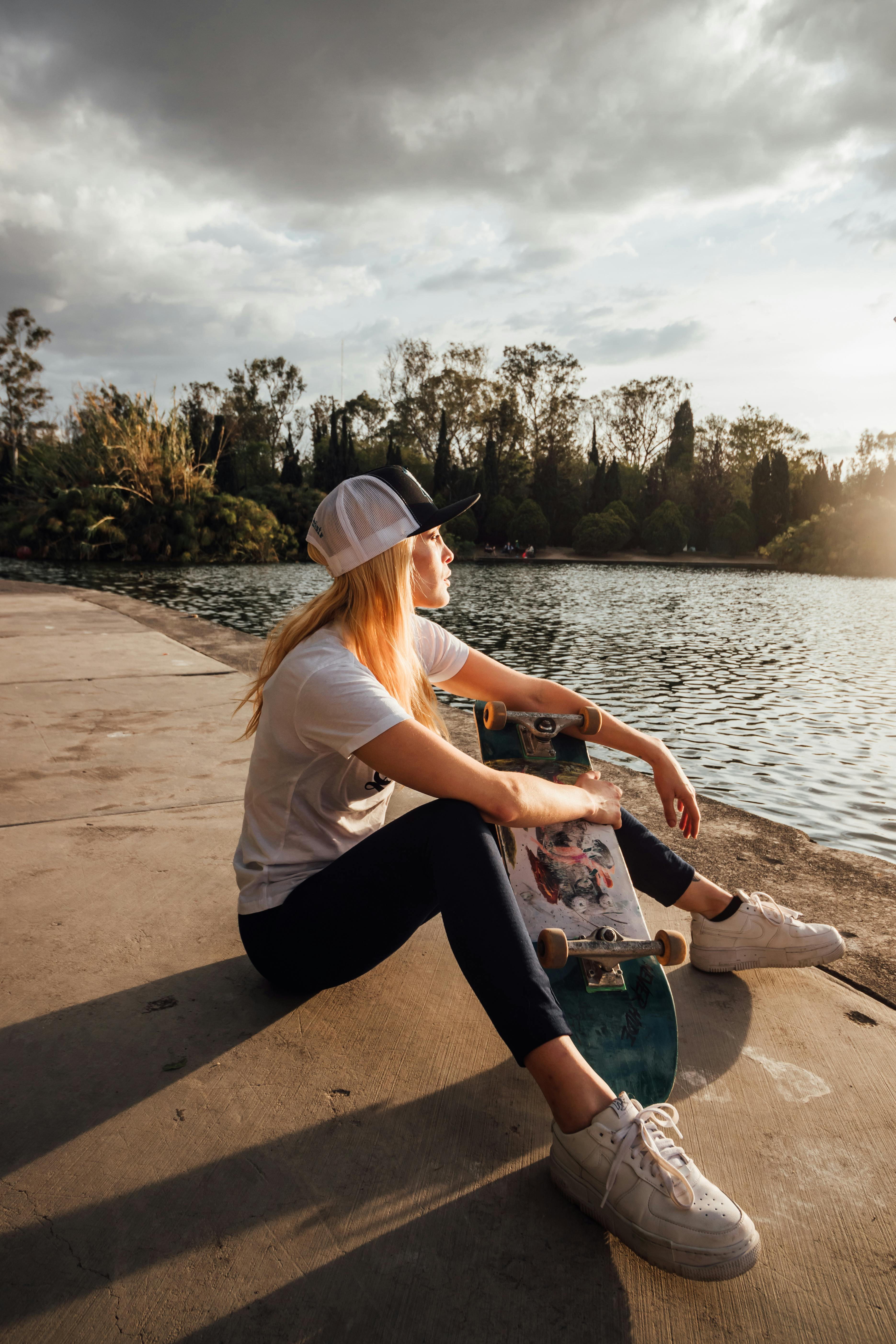 Young blonde woman wearing shorts sitting on riverbank, putting on