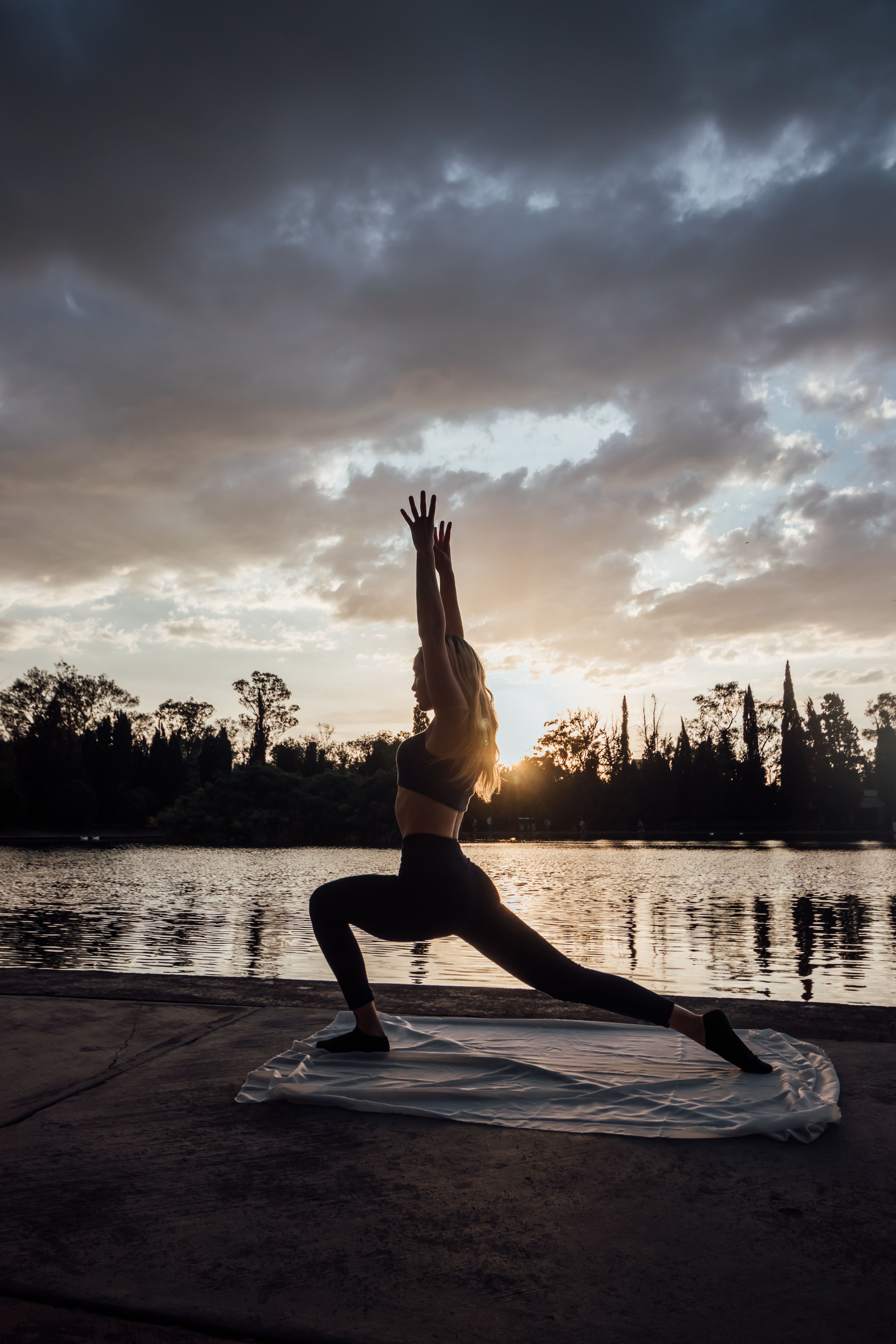 A woman performs yoga by a lakeside during a picturesque sunset, reflecting tranquility and fitness.