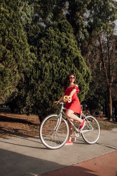 Free Woman in red dress with bicycle and sunflowers enjoying a sunny day in a park. Stock Photo