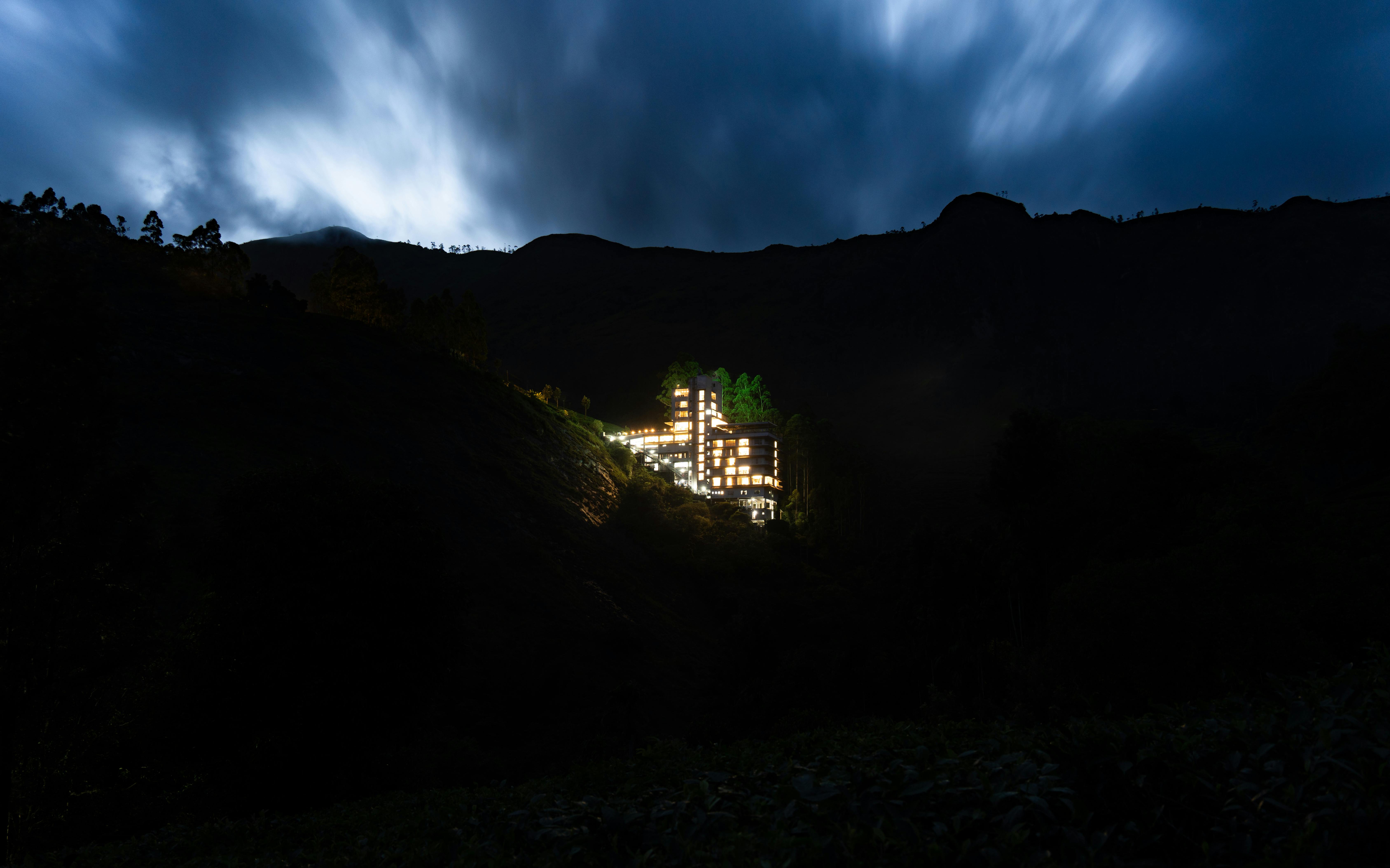 An isolated hotel glowing in an Indian mountain landscape under a dynamic night sky.