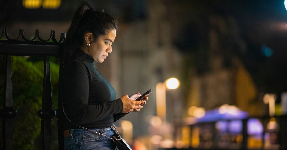 Hispanic woman comparing auto insurance quotes on smartphone in Lubbock Texas street