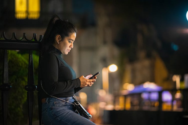 Woman Using Phone On A Street At Night