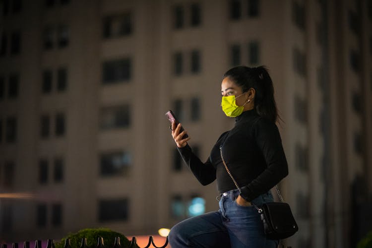 Woman In A Mask Using Phone On A Street At Night