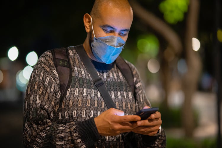 Man With Mask Using A Phone In A Street At Night