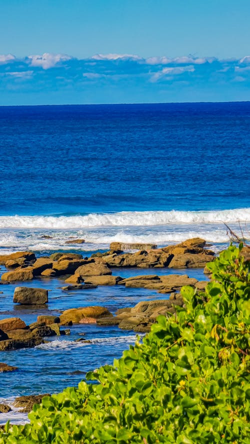 Crashing Waves Near Rocks Under a Blue Sky