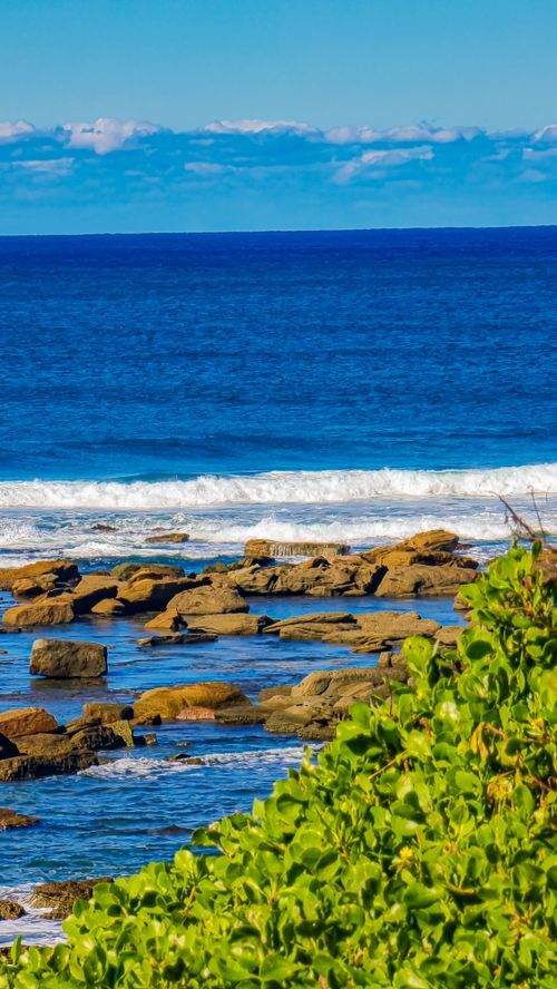 Free Breathtaking coastal scene with rocks and lush greenery under a vibrant blue sky. Stock Photo