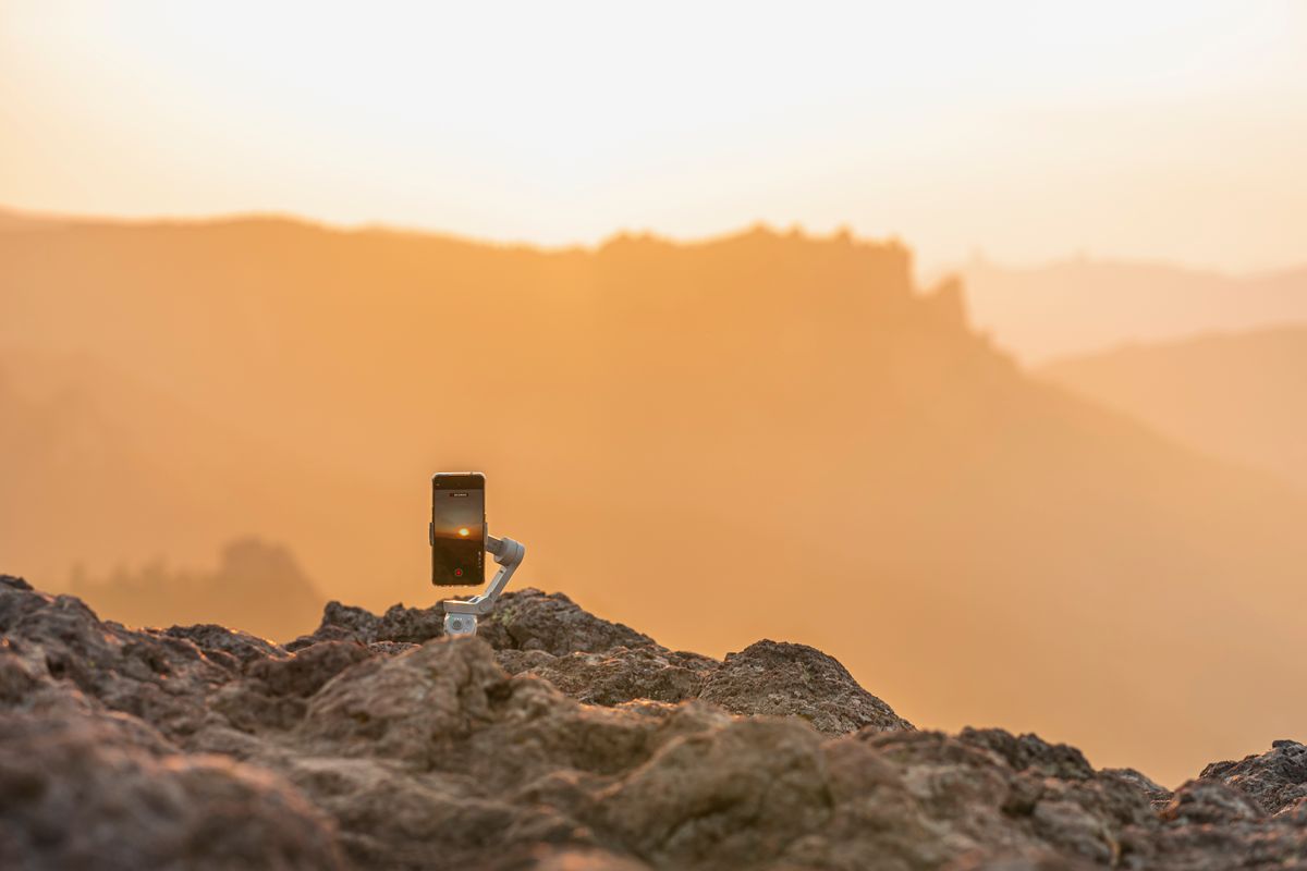 Telefon pe gimbal asezat pe o stanca, la rasarit auriu
