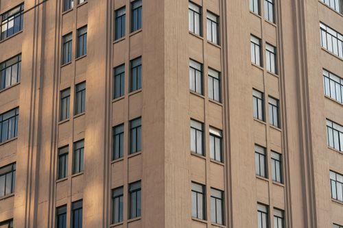 Free Close-up of a modern high-rise building showcasing concrete structure and reflective glass windows. Stock Photo