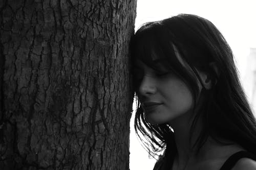 A Grayscale of a Woman Leaning Her Head on a Tree