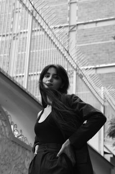 A black and white portrait of a woman confidently posing outdoors in a striped blazer.