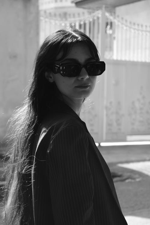 A Grayscale of a Pretty Woman Wearing a Striped Blazer and Sunglasses