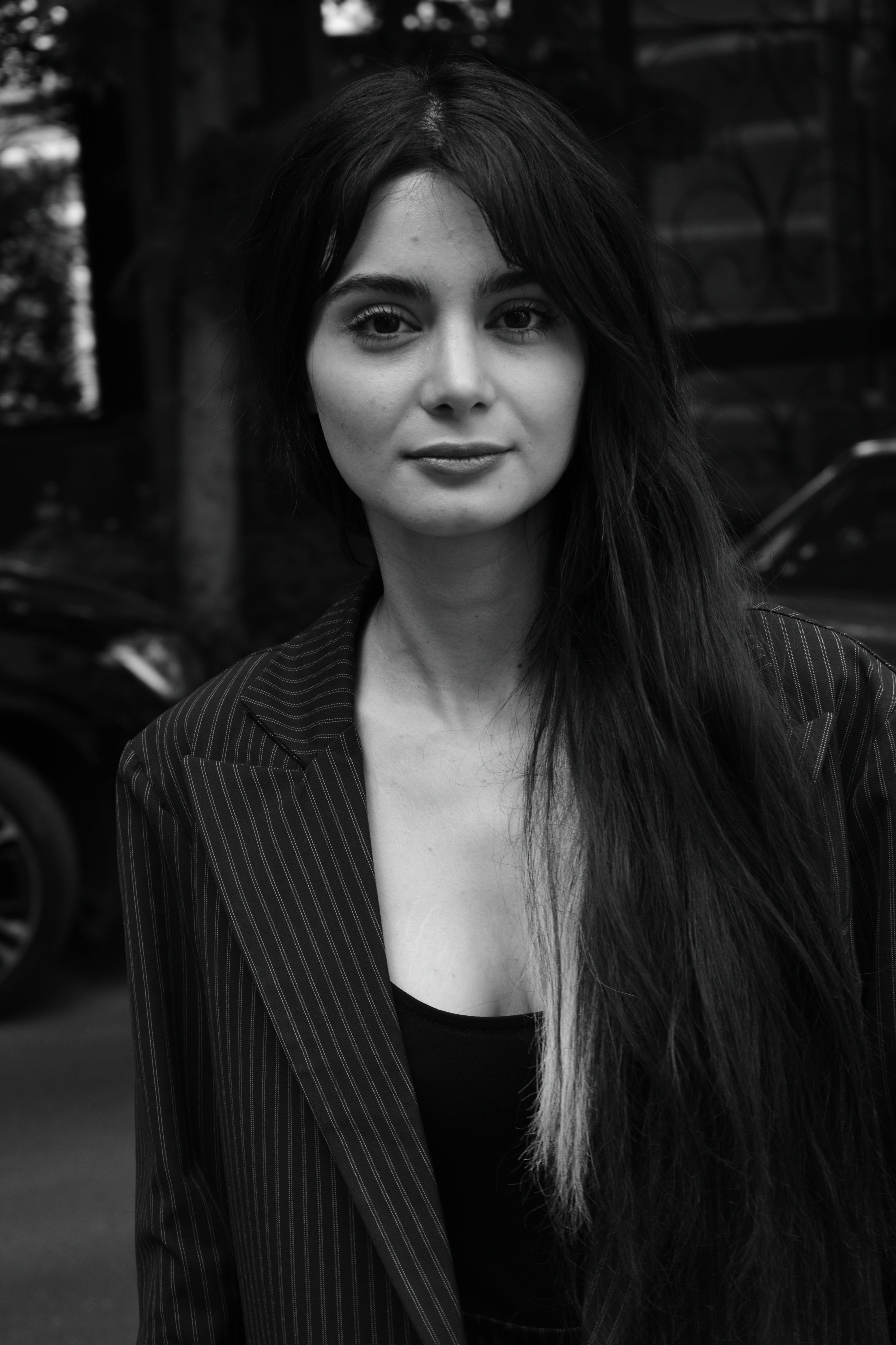 Black and white portrait of an elegant woman with long hair in a striped blazer outdoors.