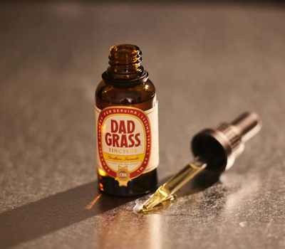 Close-up image of a Dad Grass tincture bottle and dropper against a neutral background.