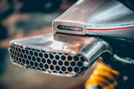 特写展示了一款带有意大利国旗装饰带的现代摩托车排气装置，其复杂的工程与设计清晰可见