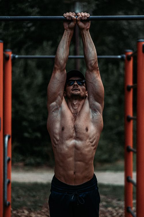 Free Muscular man doing pull-ups on outdoor gym equipment, showcasing strength and fitness. Stock Photo