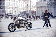 一辆时尚摩托车停在罗马繁忙的广场上，捕捉着城市生活与建筑的气息