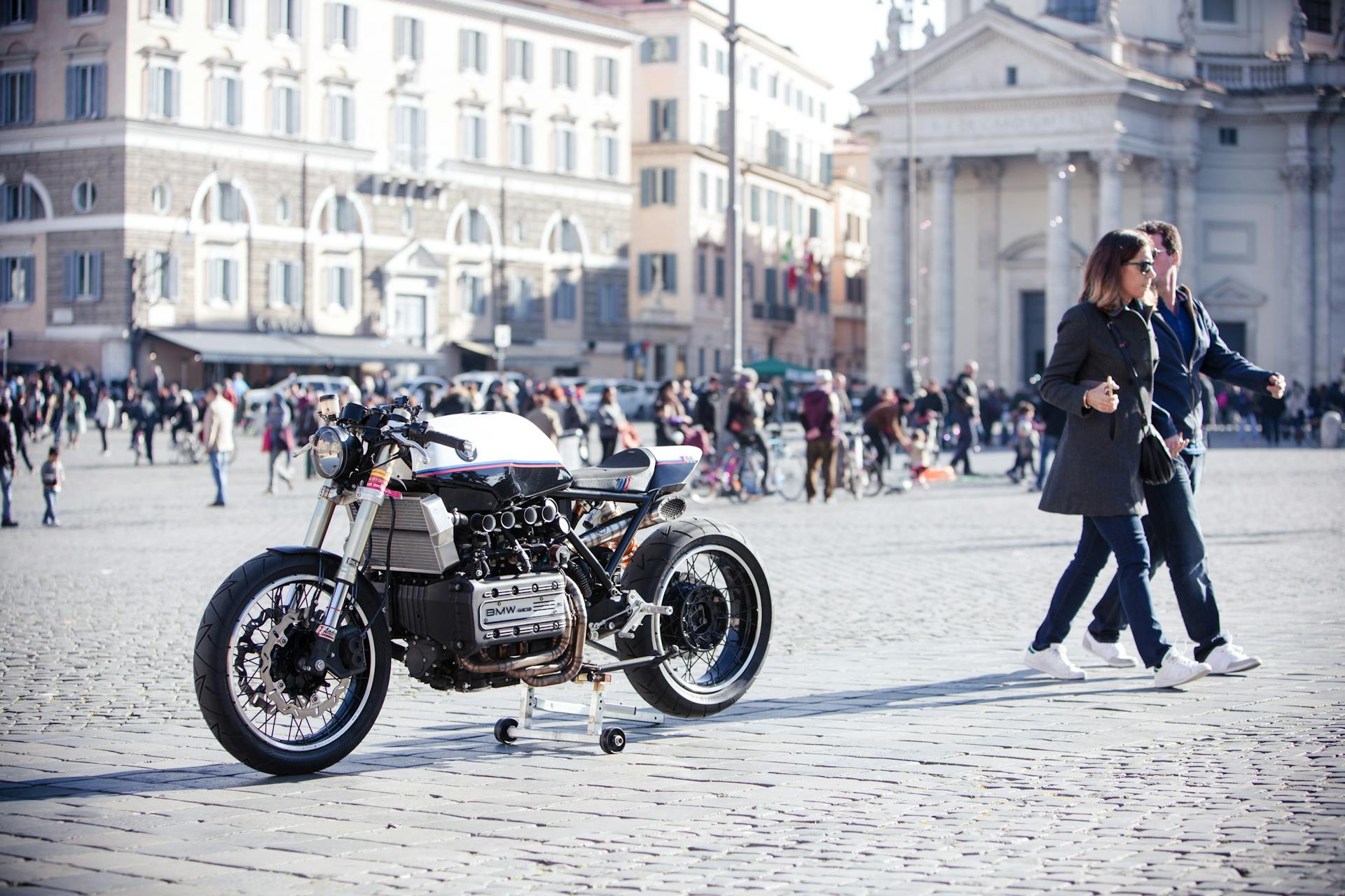 Stylish motorcycle parked in a busy square in Rome, capturing urban life and architecture.