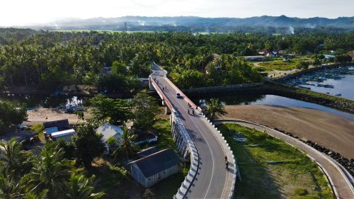 Free Aerial shot of a bridge crossing a river in lush greenery, with a view of Pangandaran, Indonesia. Stock Photo