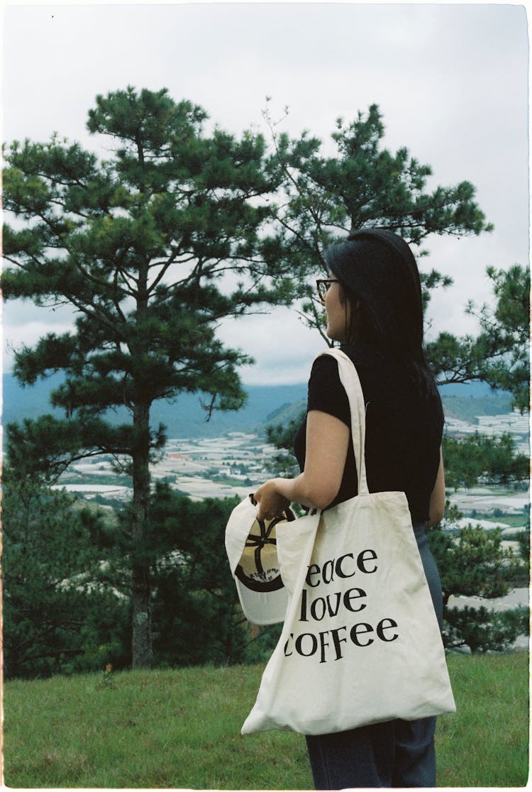 A Woman In Black Shirt Carrying A White Tote Bag And Cap