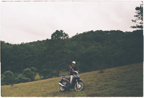 Free A person on a motorbike pauses on a picturesque hillside with lush greenery. Stock Photo