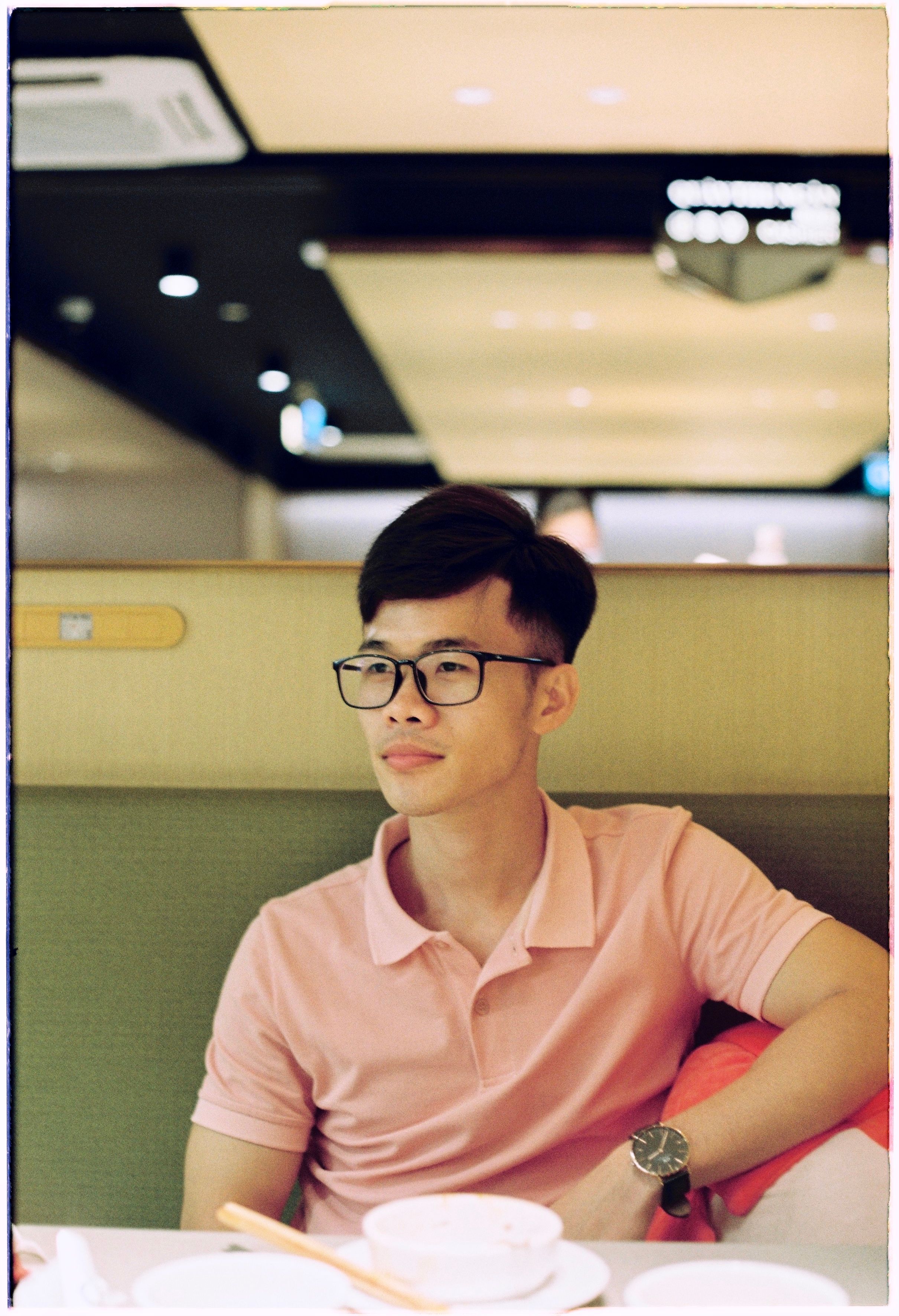 Young man with eyeglasses relaxing at a restaurant table.