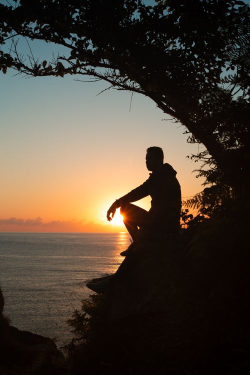 Free Silhouette of a man sitting on a cliff at sunset, capturing tranquility and natural beauty. Stock Photo