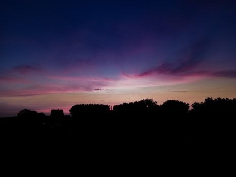 A stunning twilight sky with vibrant colors and tree silhouettes creates a serene evening scene.