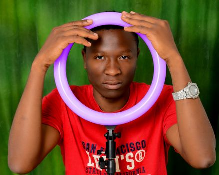 Young man holding a ring light in a modern portrait setup, wearing a casual red shirt.