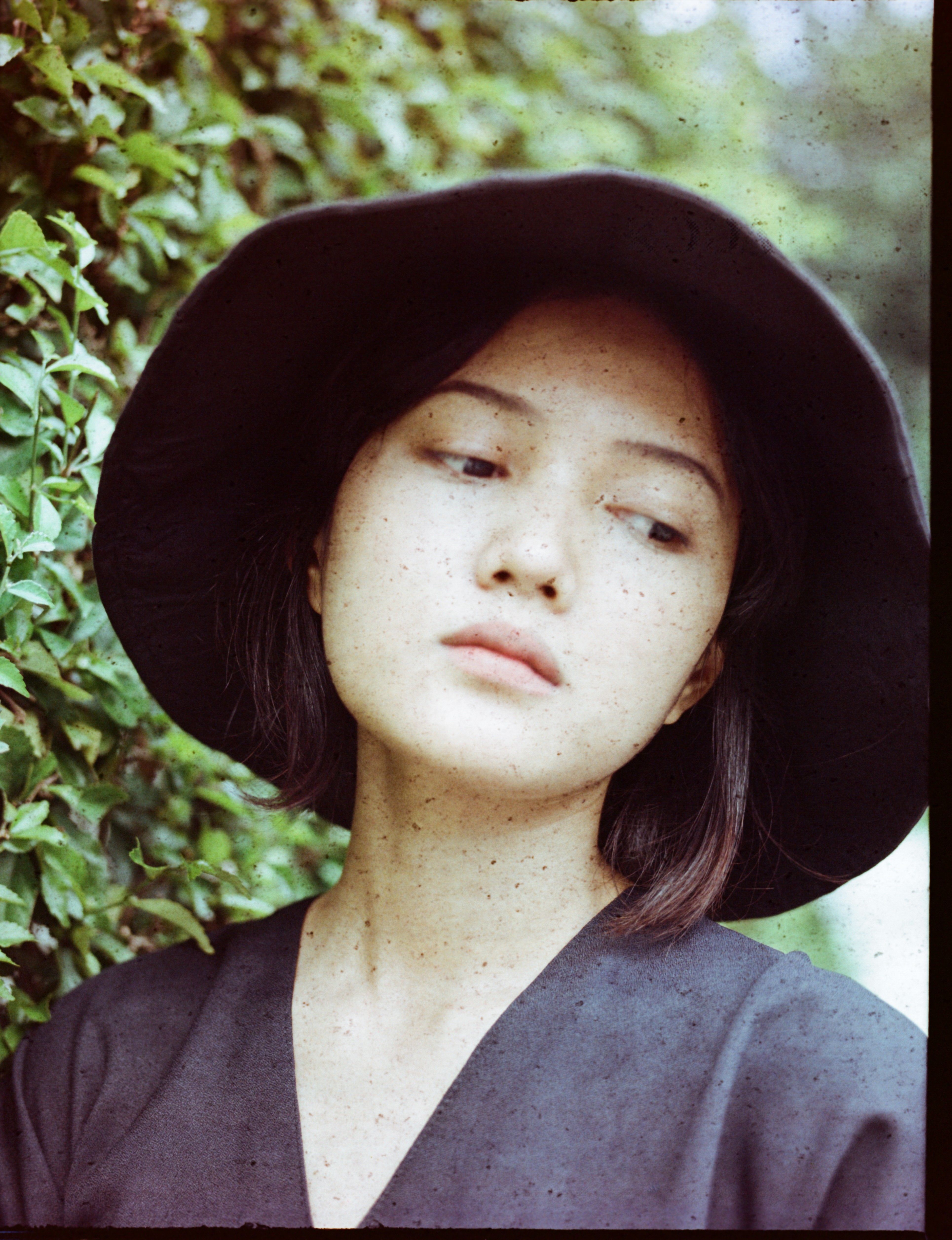 Elegant portrait of a woman in a black hat, exuding a mysterious vibe in an outdoor setting.