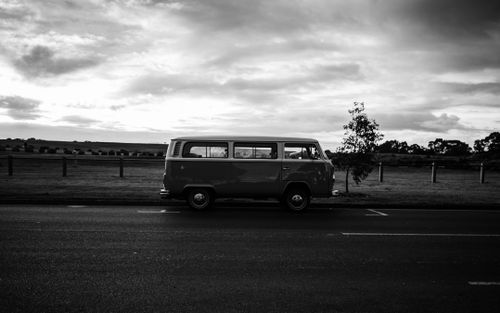 Free Black and white photo of a vintage van parked on an empty road under an overcast sky. Stock Photo