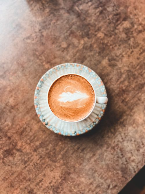 Free A top view of a cappuccino with intricate latte art in a ceramic cup on a textured table. Stock Photo