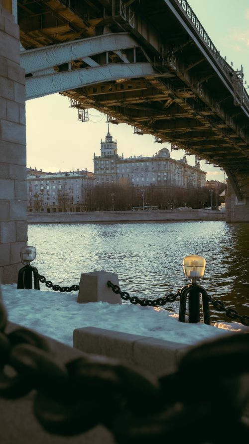 Free A scenic view of a bridge over a river with urban buildings in the background during twilight. Stock Photo