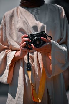 A person wearing a robe holds a vintage Zenit camera in a warm outdoor setting.