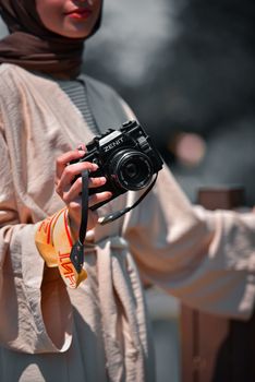 A woman in traditional attire holding a camera, showcasing a blend of modern and classic style.